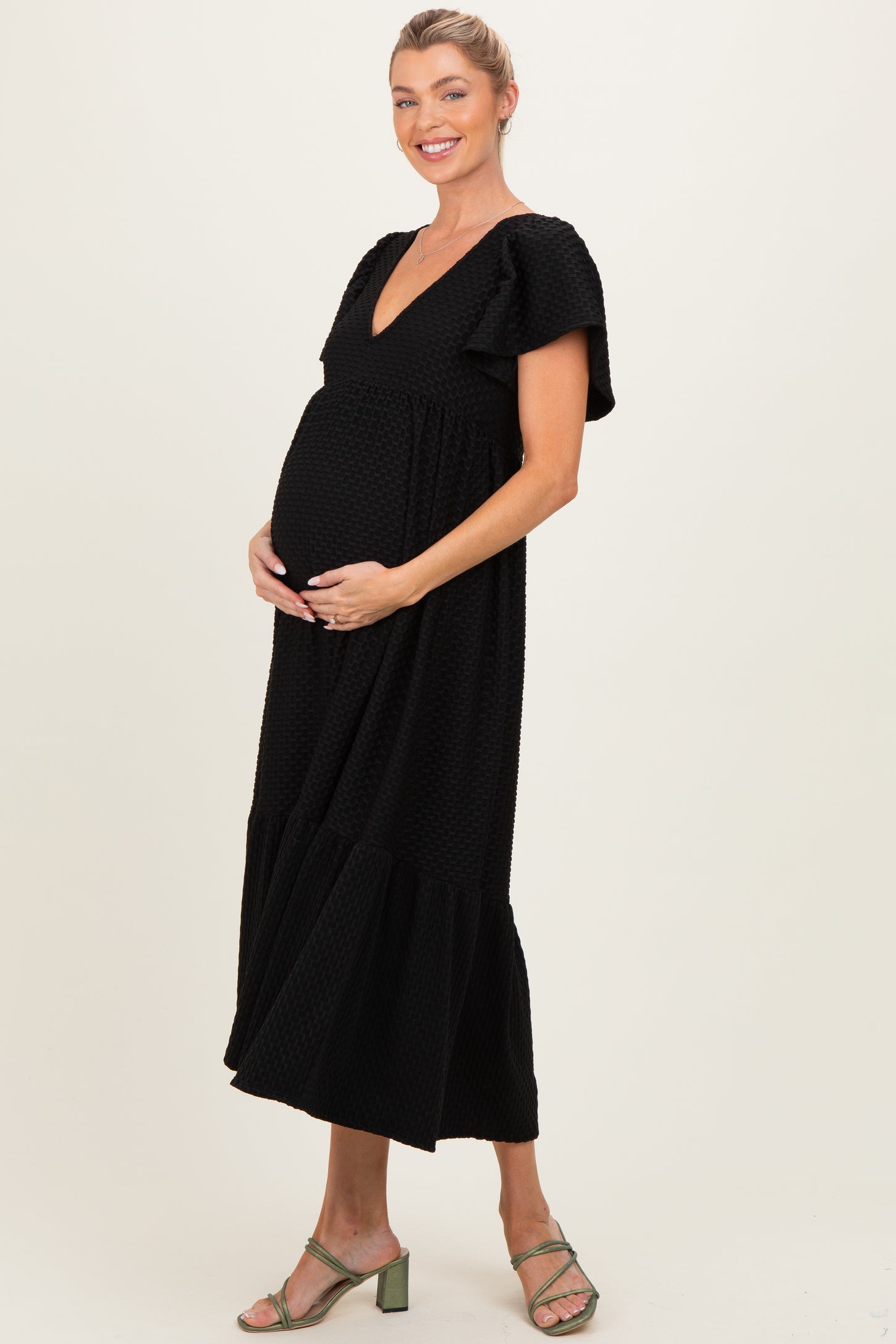 woman wearing a black maternity maxi dress with flutter sleeves and a v-neck, showcasing her baby bump