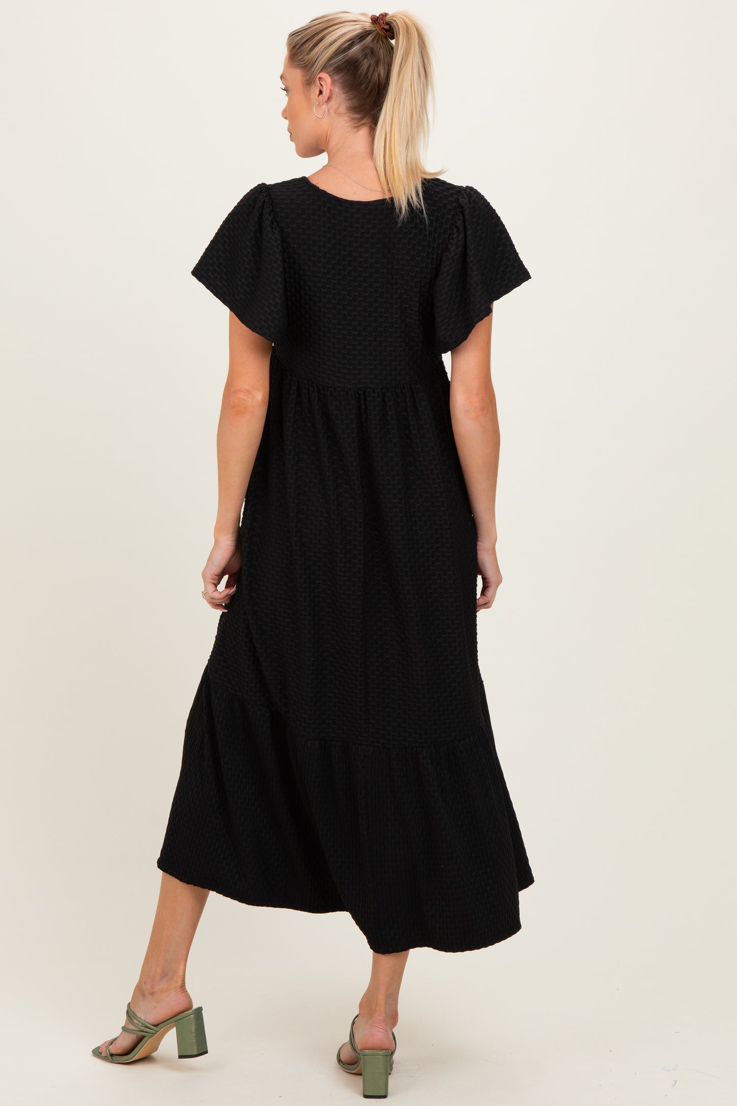 woman wearing a black maternity maxi dress with a tiered skirt and flutter sleeves, showing her back