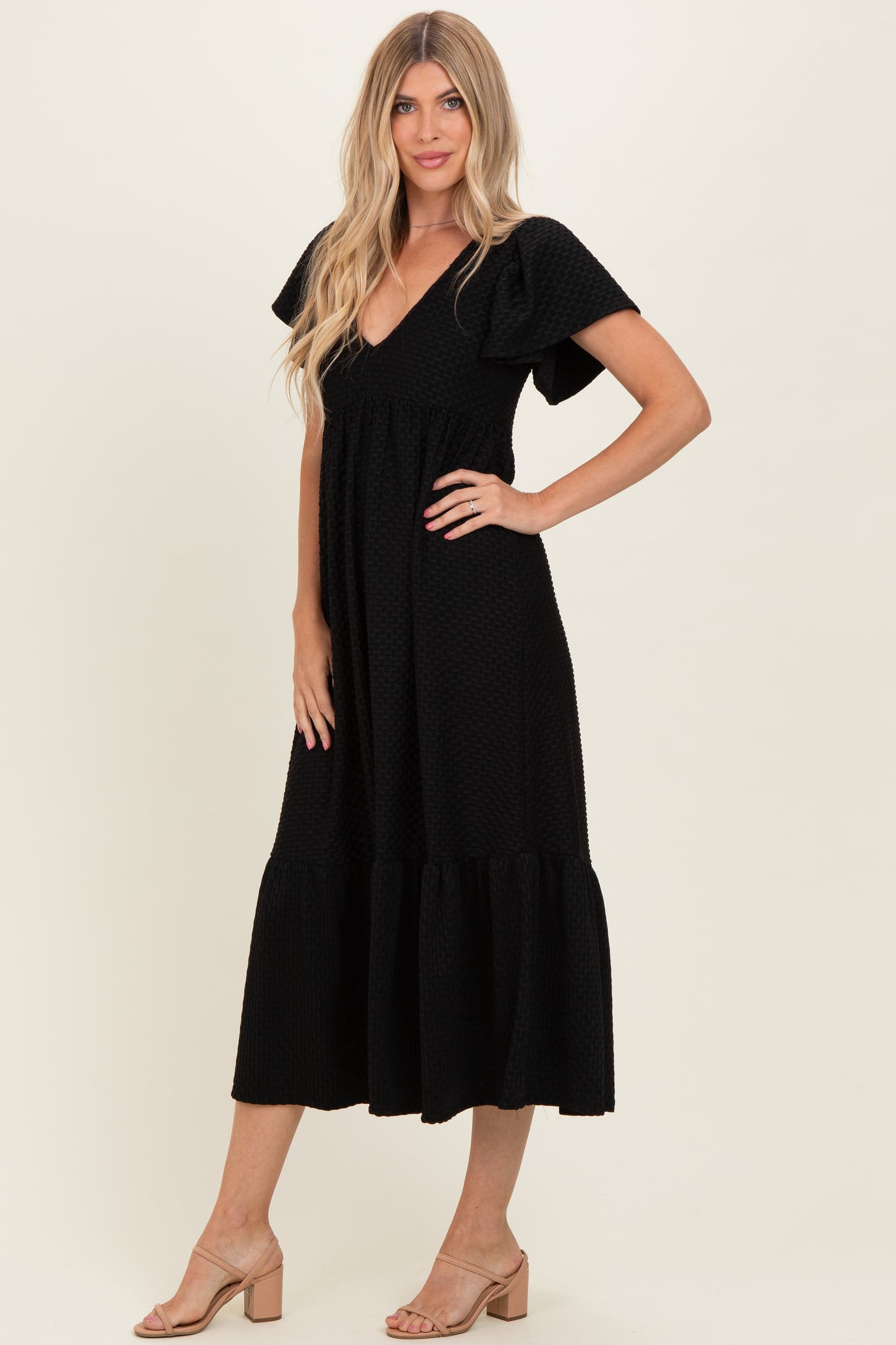 woman wearing a black midi dress with flutter sleeves and a tiered hem, standing in a relaxed pose
