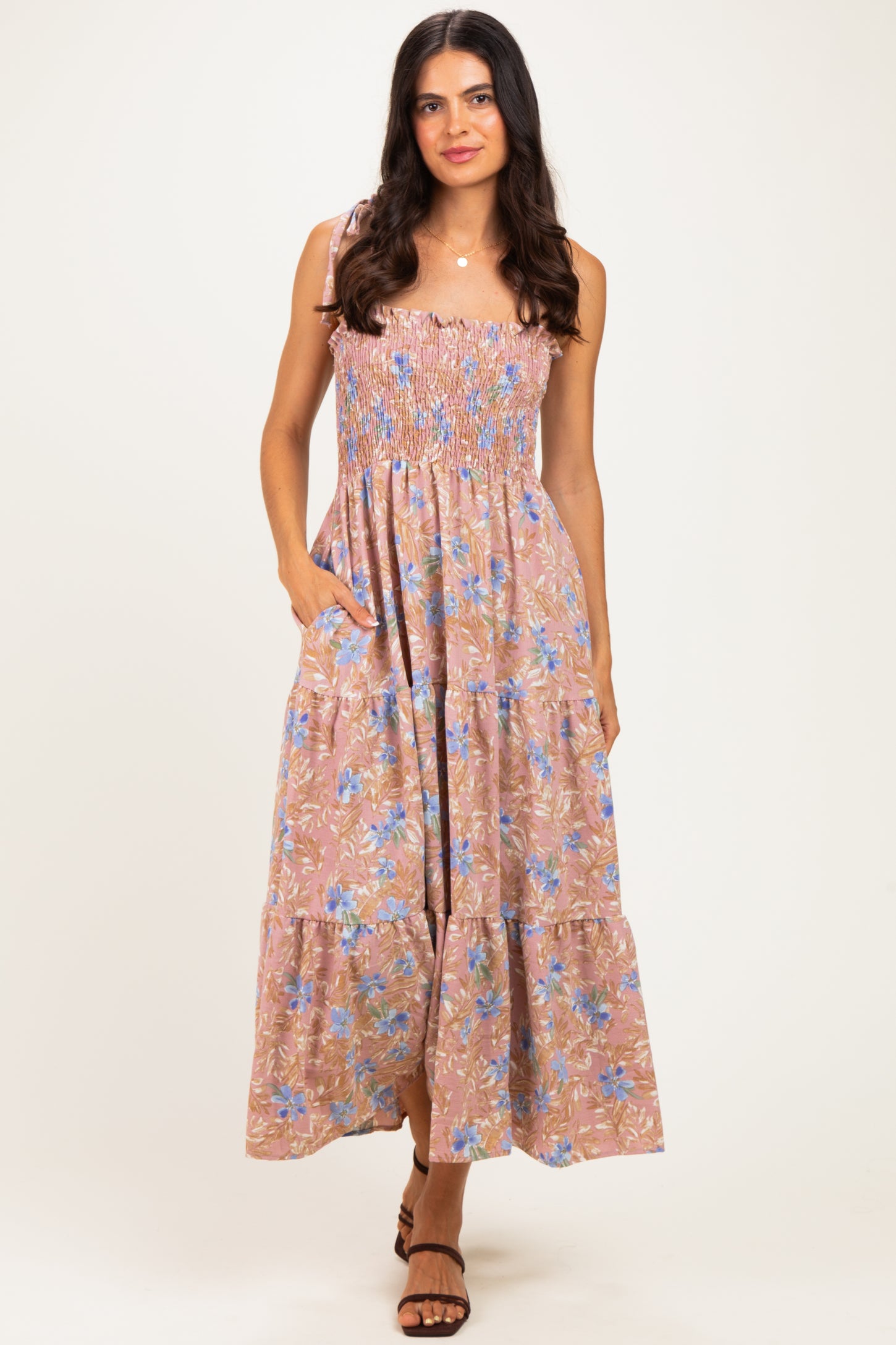 woman wearing a pink floral maxi dress with smocking detail and pockets, standing against a neutral background