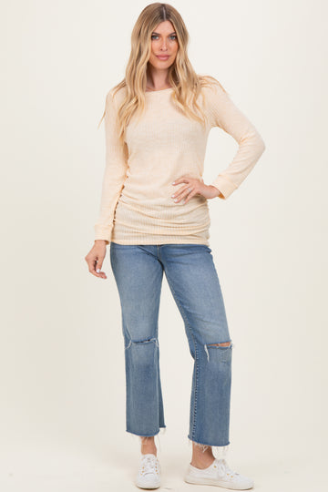 woman wearing a light peach long sleeve ribbed top and distressed blue jeans with white sneakers