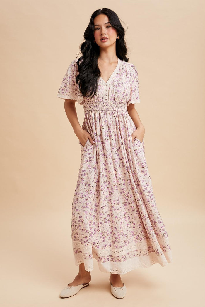 woman wearing a floral print maxi dress with short sleeves and pockets, standing against a neutral background