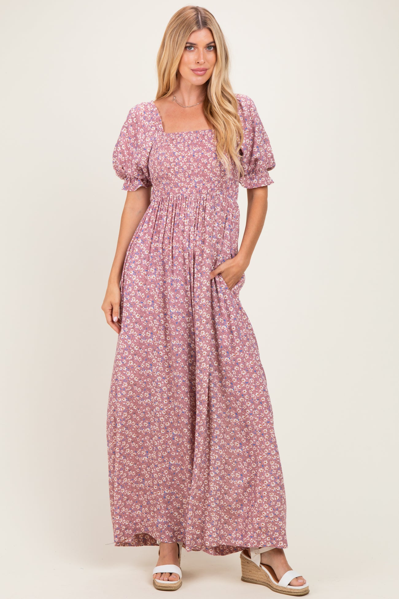 woman wearing a purple floral maxi dress with square neckline and puff sleeves, standing with hands in pockets
