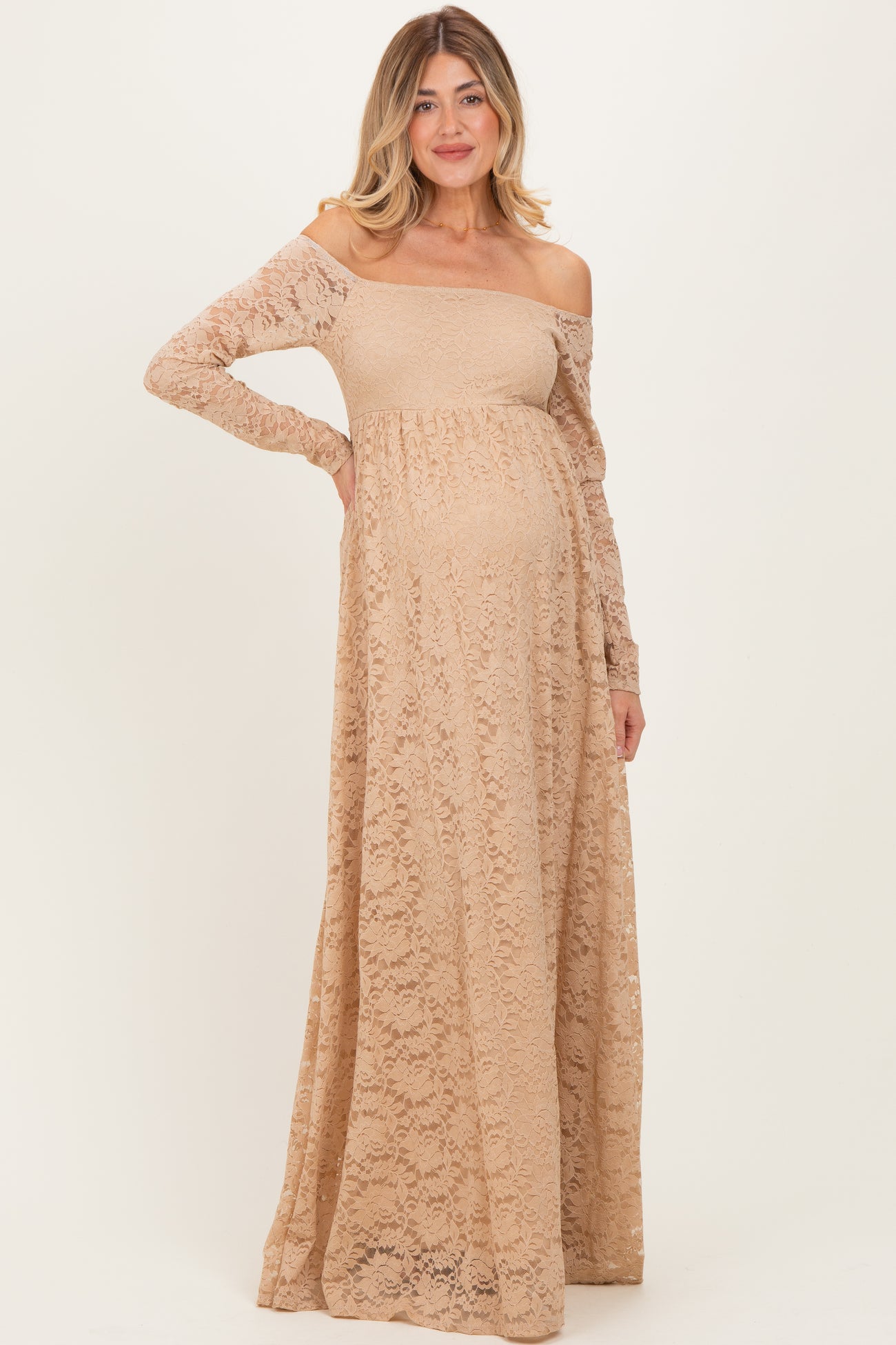 woman wearing a beige lace off-shoulder maternity gown with long sleeves and a visible baby bump