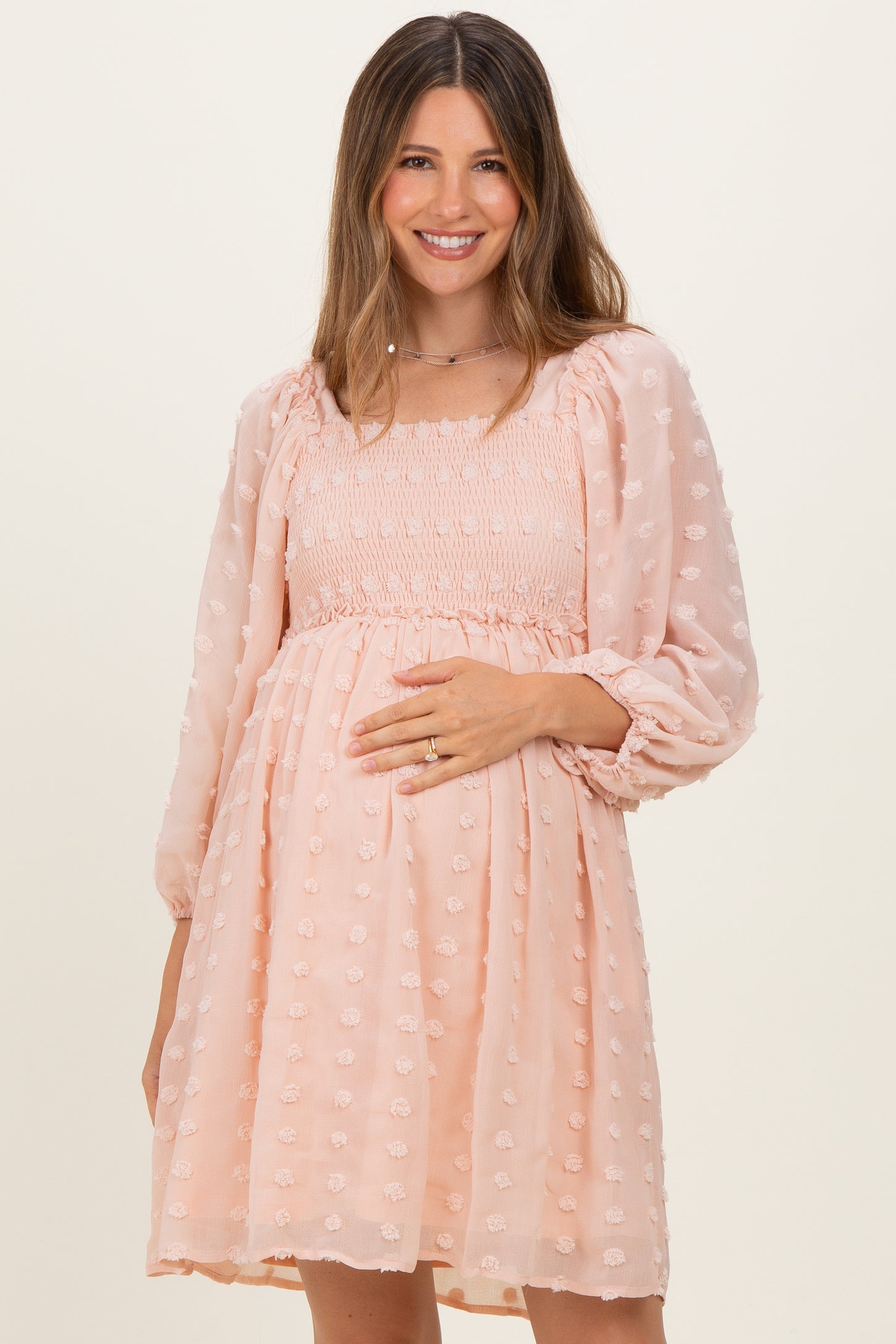 woman wearing a light pink maternity dress with smocked bodice and puff sleeves, holding her baby bump