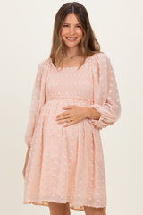 woman wearing a light pink maternity dress with smocked bodice and puff sleeves, holding her baby bump