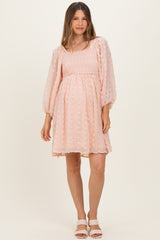 woman wearing a light pink maternity dress with puff sleeves and a smocked bodice, standing in a relaxed pose