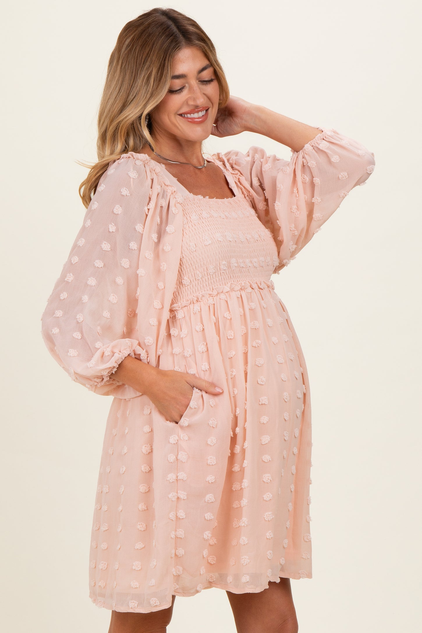 woman wearing a light peach maternity dress with puff sleeves and floral details, showing her baby bump