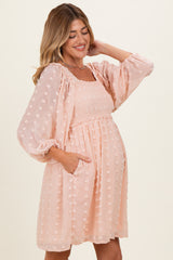 woman wearing a light peach maternity dress with puff sleeves and floral details, showing her baby bump