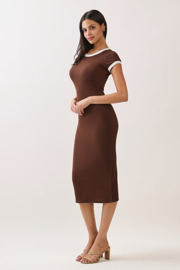 woman wearing a brown fitted midi dress with white trim and strappy heels, standing with hands clasped in front