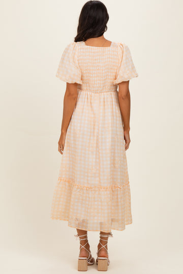 woman wearing a light orange and white gingham smocked maxi dress with puff sleeves and ruffle hem