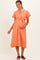 woman wearing a coral maternity dress with short sleeves, button details, and a tie belt, holding her baby bump