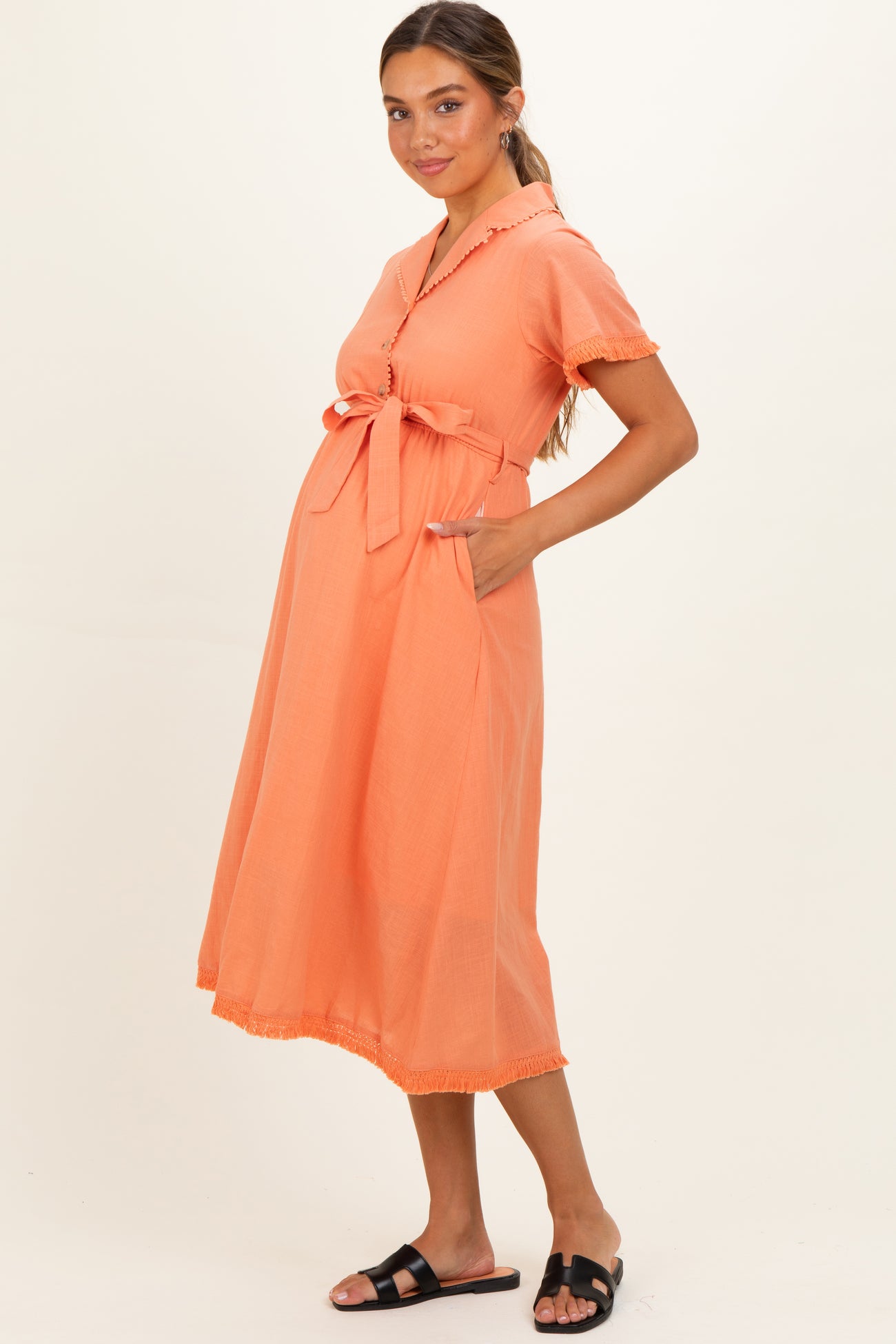woman wearing an orange maternity dress with a tied waist and pockets, featuring short sleeves and a flared skirt, showing baby bump