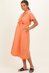 woman wearing an orange maternity dress with a tied waist and pockets, featuring short sleeves and a flared skirt, showing baby bump