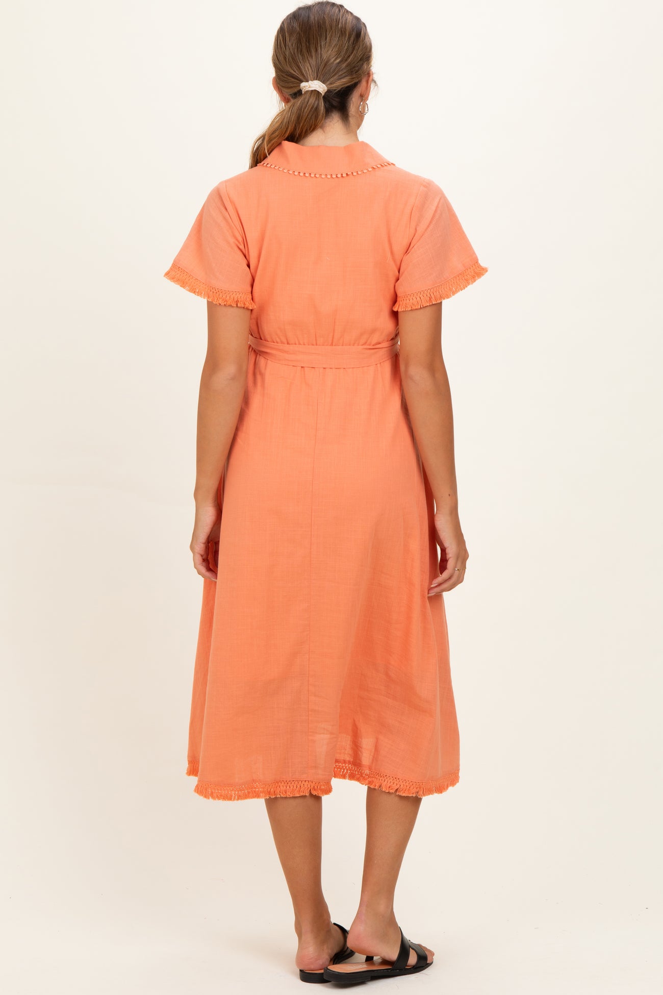 woman wearing an orange maternity dress with short sleeves and fringe detailing, shown from the back