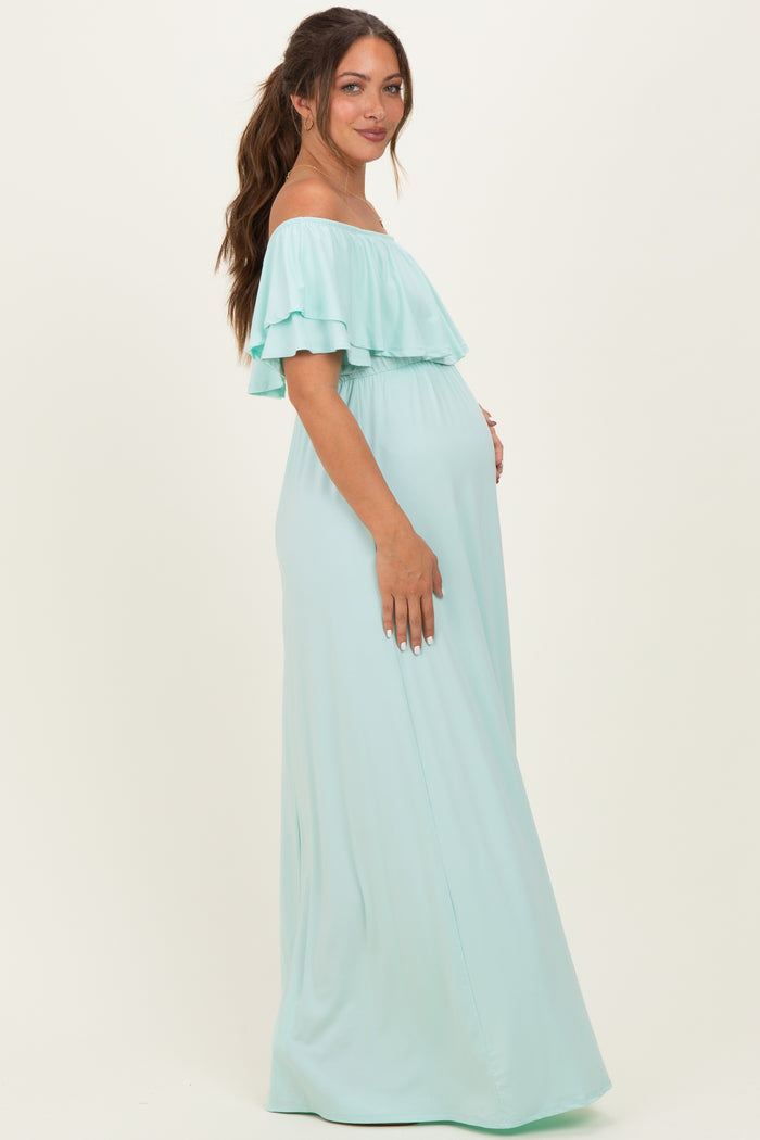 woman wearing a light mint green off-the-shoulder maternity maxi dress with ruffle details and showing her baby bump