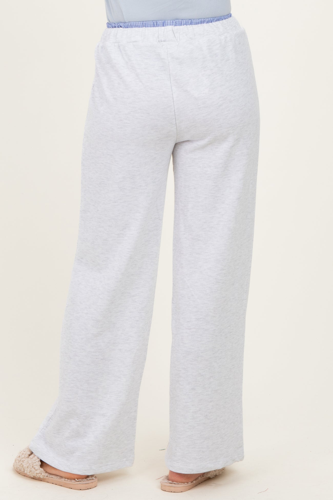 woman wearing light grey wide-leg lounge pants with an elastic waistband and light blue accent, standing with back to camera