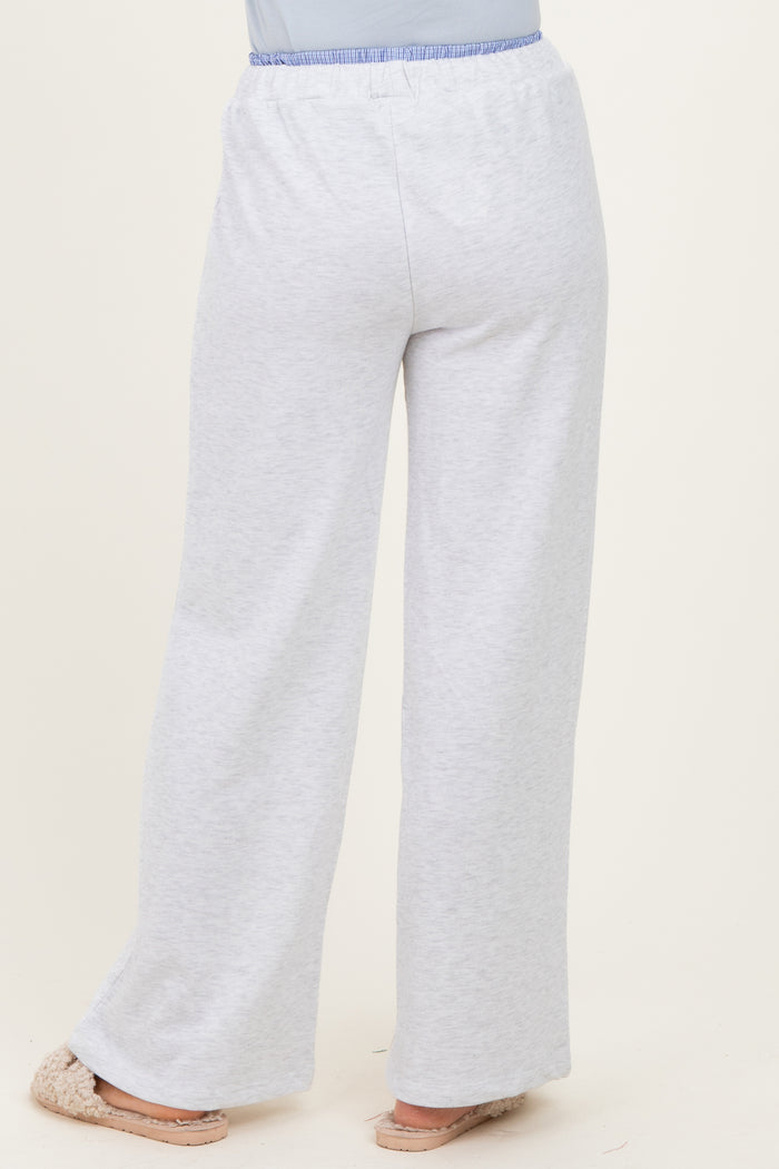 woman wearing light grey wide-leg lounge pants with an elastic waistband and light blue accent, standing with back to camera