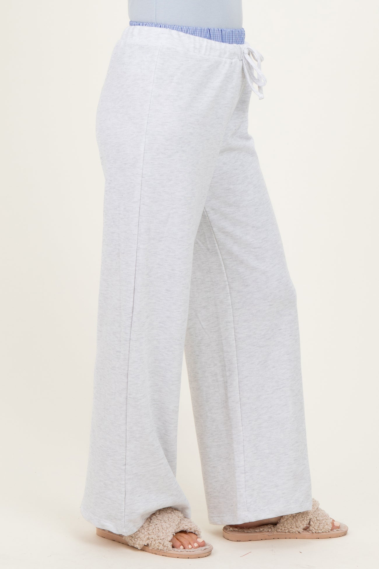 woman wearing light gray wide-leg sweatpants with an elastic waistband and drawstring detail, paired with cozy slippers