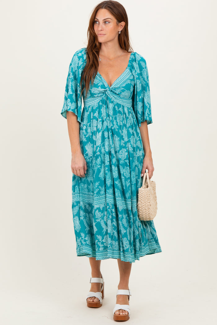 woman wearing a turquoise floral maxi dress with short sleeves and a v-neckline, holding a woven handbag