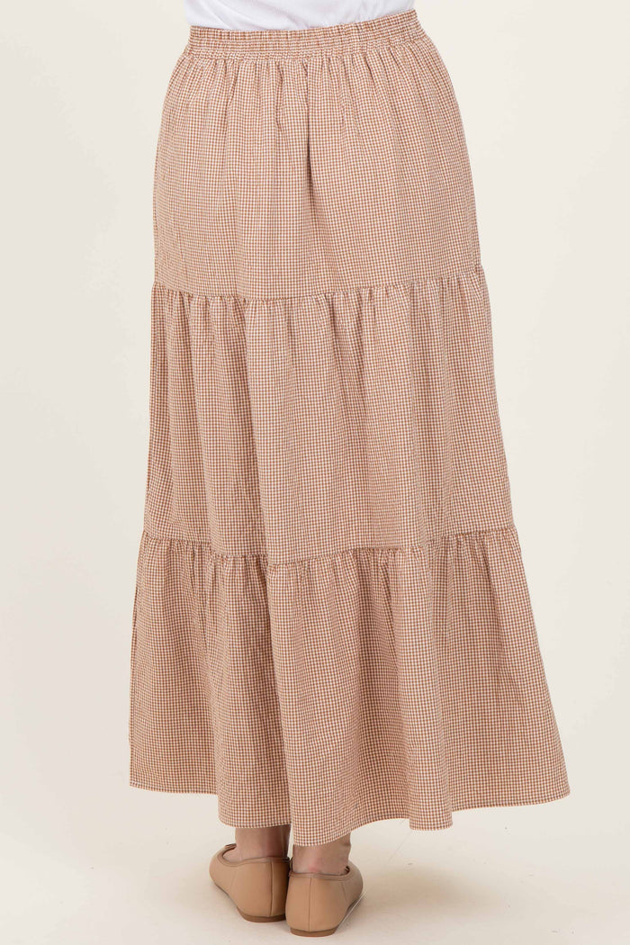 woman wearing a tiered maxi skirt in a brown and cream checked pattern, featuring an elastic waistband and flowing style