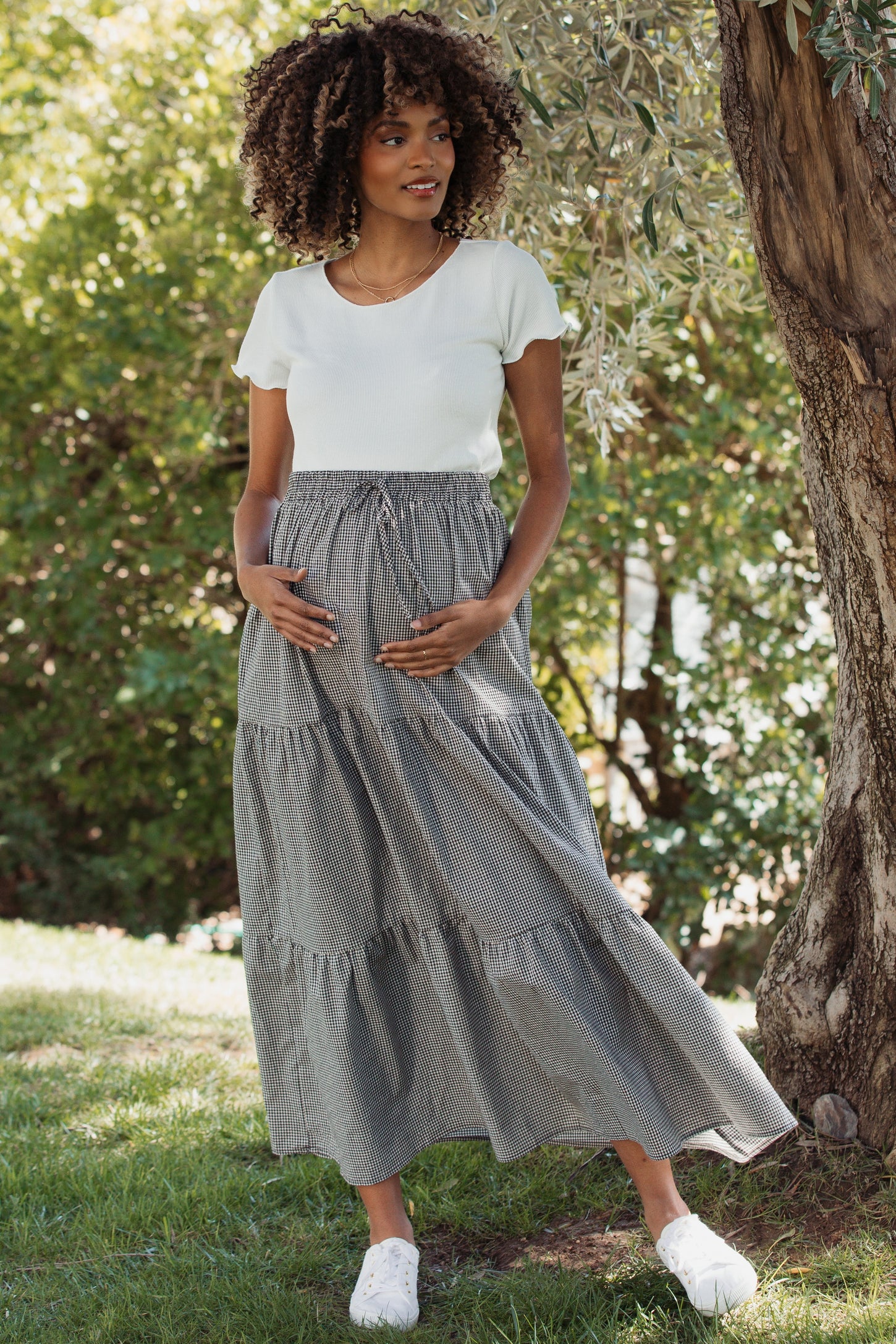 woman wearing a white ribbed short sleeve top and a black and white striped tiered maternity skirt, holding her baby bump