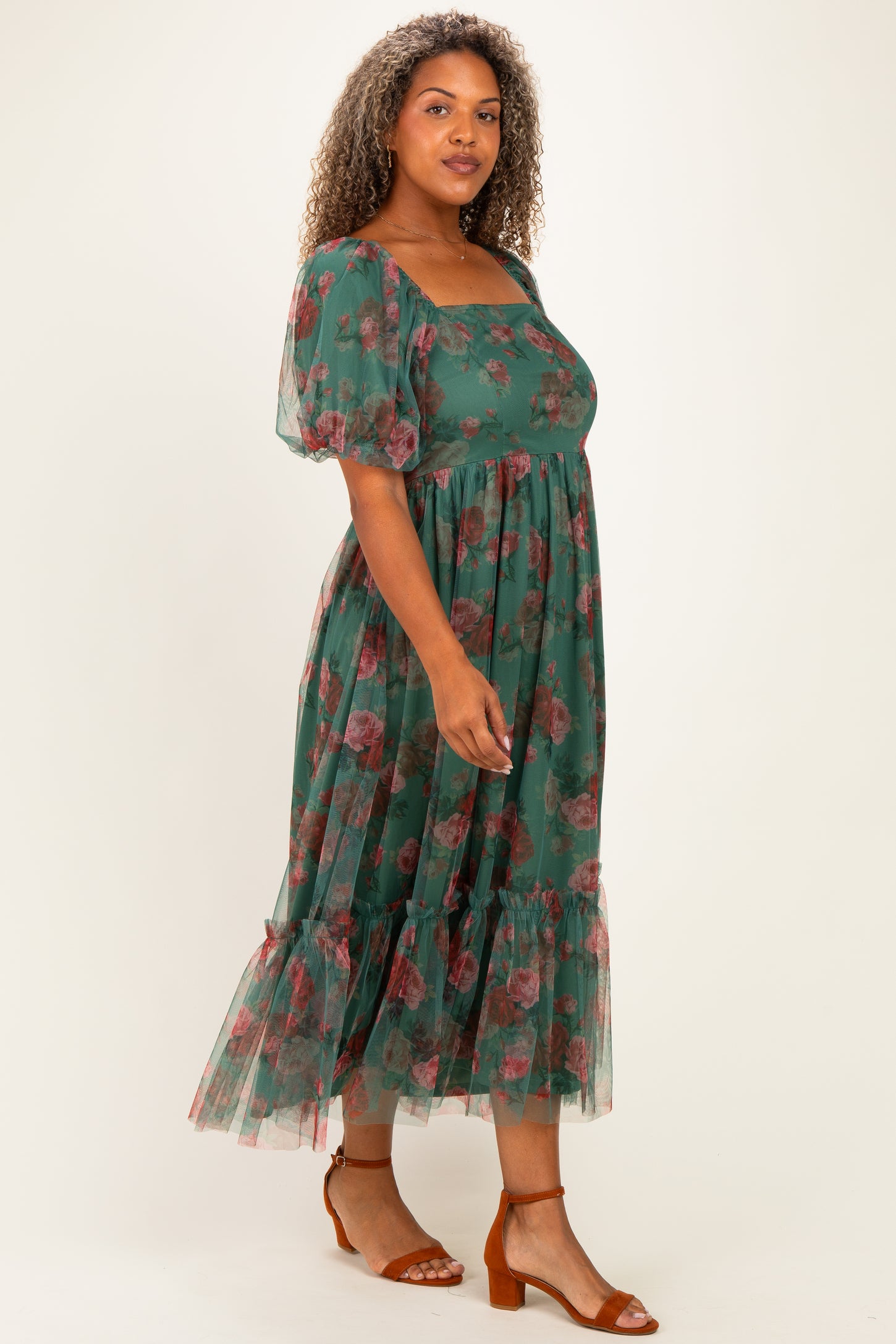 woman wearing a green floral plus-size maxi dress with puff sleeves and a tiered hem, standing on a light background