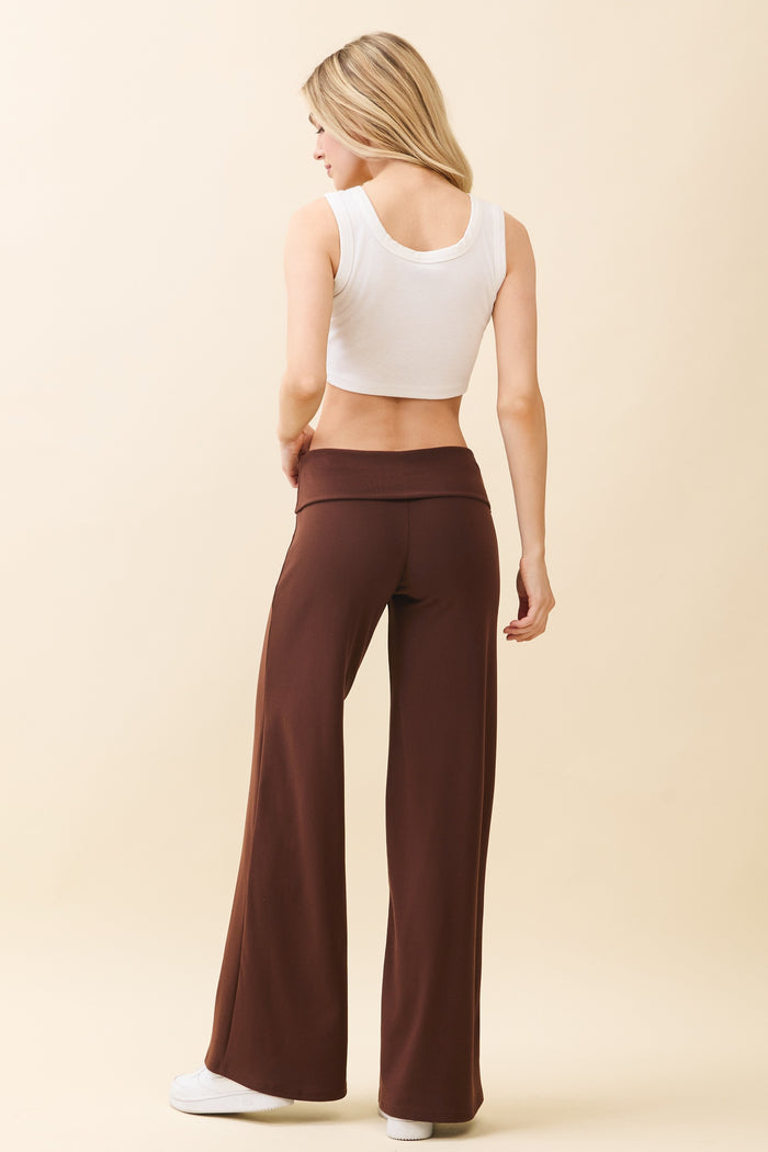 woman wearing a white crop top and brown wide-leg pants, viewed from the back against a neutral background