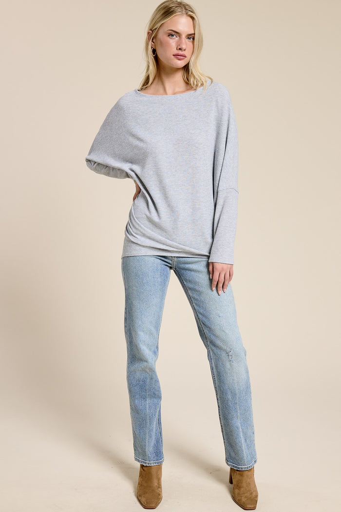 woman wearing a light gray oversized sweater with a boat neckline and blue straight-leg jeans