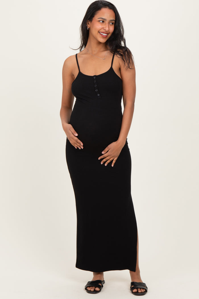 woman wearing a black ribbed maternity maxi dress with buttons and side slits, gently cradling her baby bump