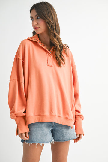 woman wearing a loose-fitting peach long sleeve pullover with a collar and paired with denim shorts