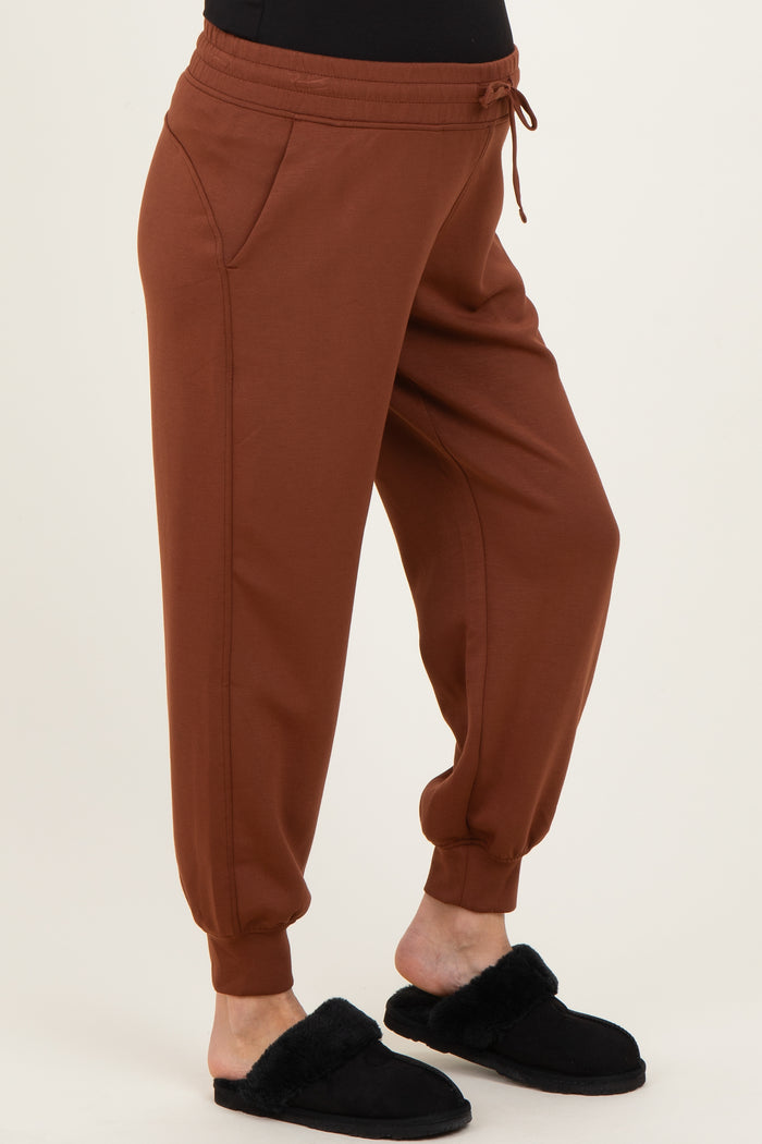 maternity wear rust colored joggers with side pockets and elastic cuffs, model wearing black slippers