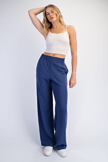 woman wearing a white spaghetti strap crop top and loose navy blue sweatpants, standing with one hand on her hip