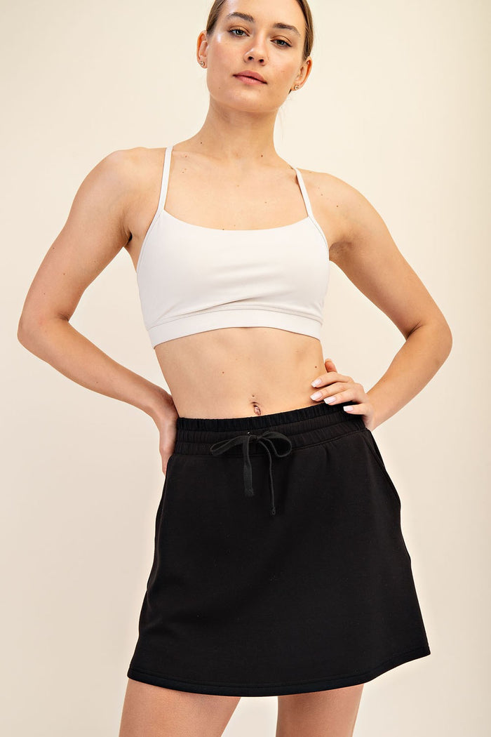 woman wearing a white cropped sports bra and a black drawstring skirt