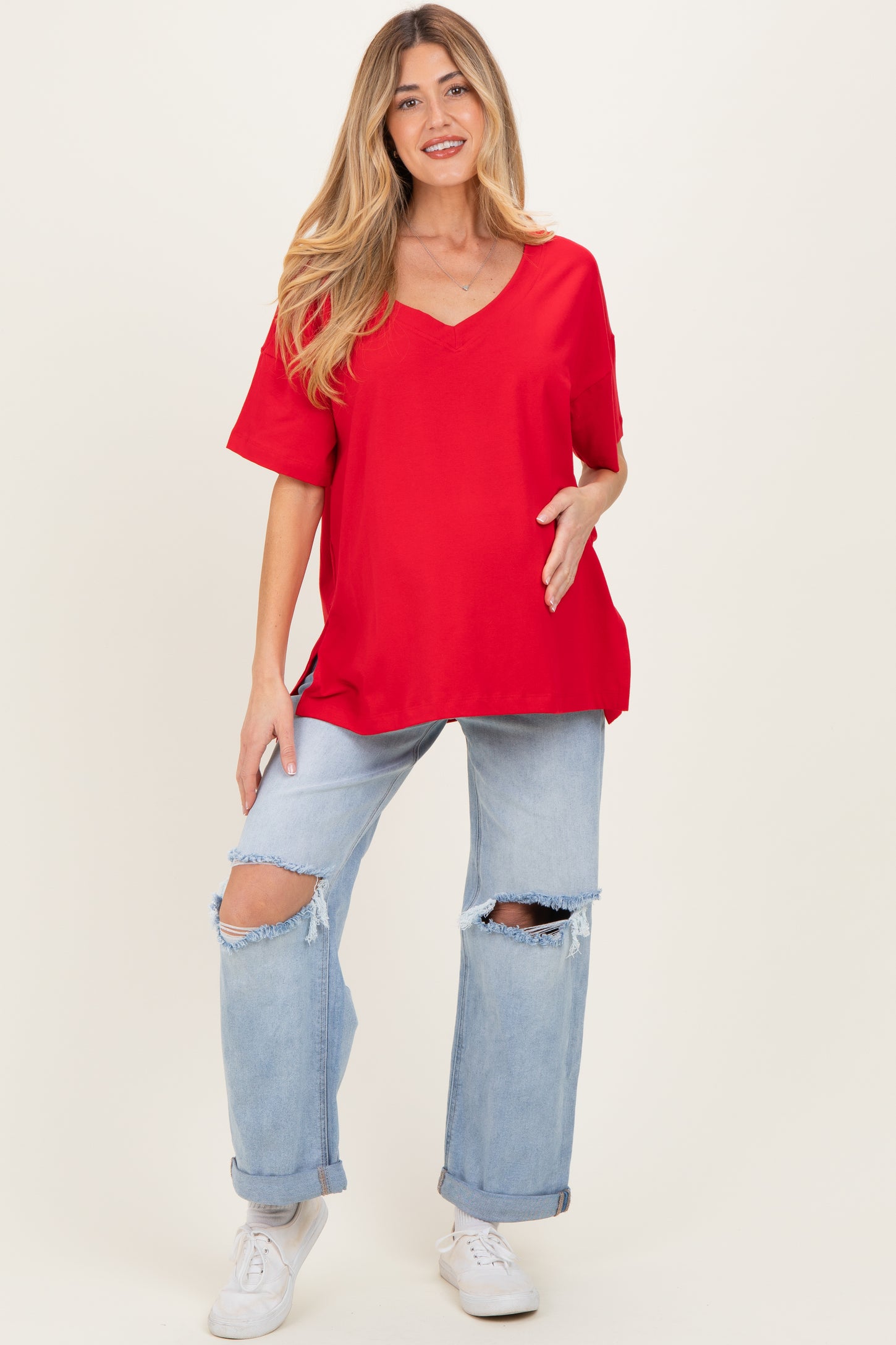 woman wearing a red v-neck maternity top and distressed light blue jeans, showing her baby bump