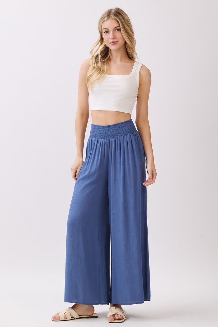 woman wearing a white cropped tank top and flowy blue wide-leg pants with an elastic waistband