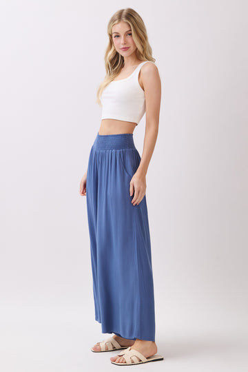 woman wearing a white crop top and flowy blue maxi skirt with a smocked waistband