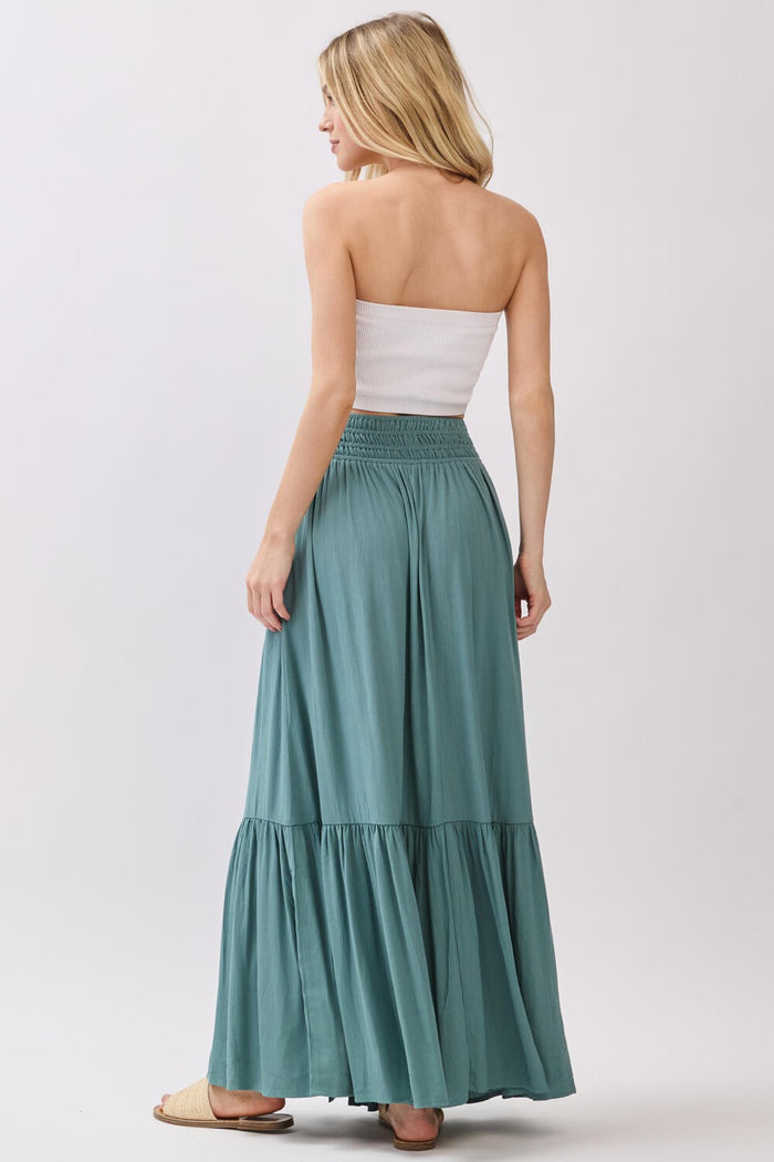 woman wearing a light green maxi skirt with a tiered design and a white strapless top, viewed from the back
