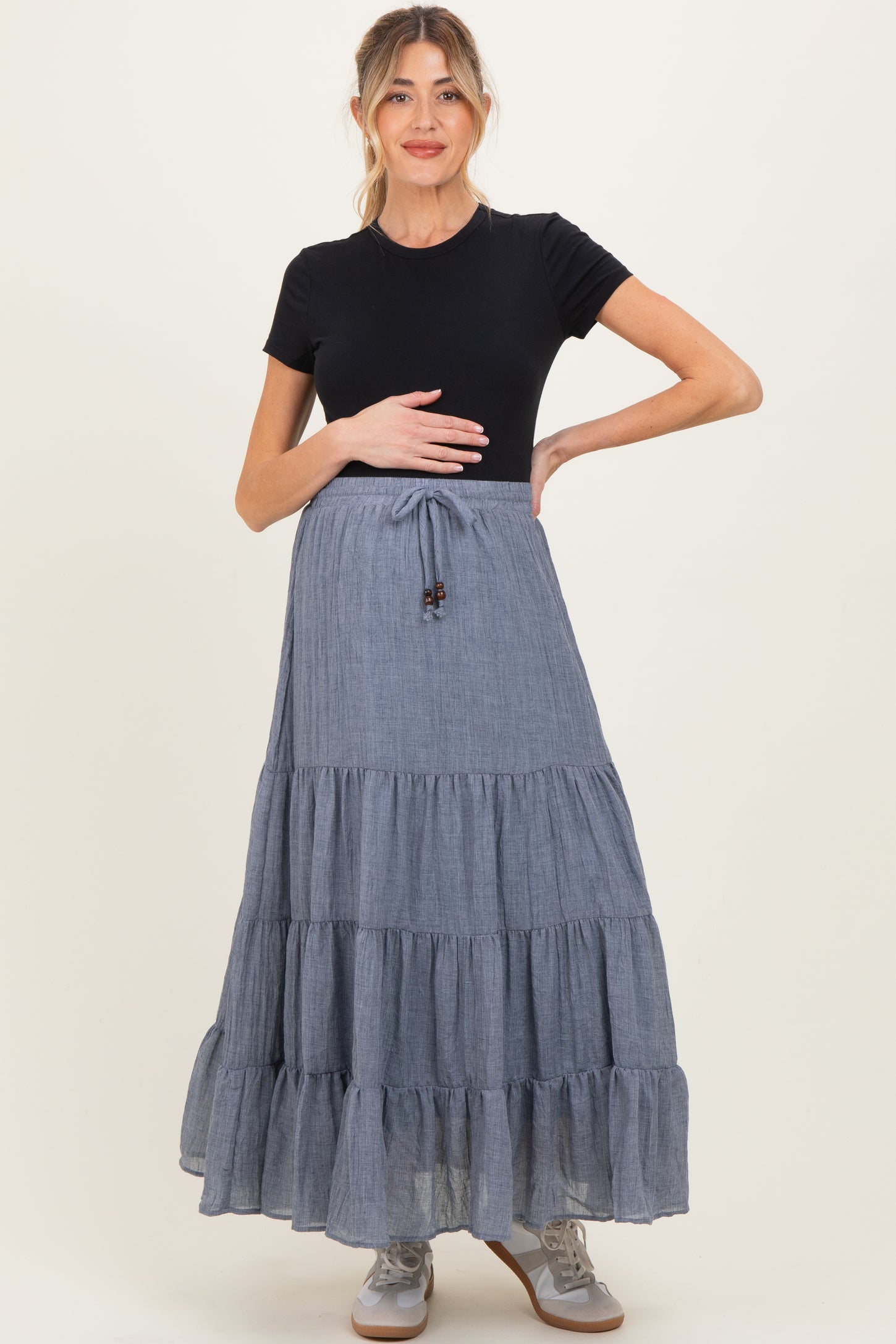 woman wearing a black short sleeve maternity top and a blue tiered maxi skirt, holding her baby bump
