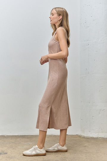 woman wearing a beige sleeveless maxi dress with a side slit and white sneakers