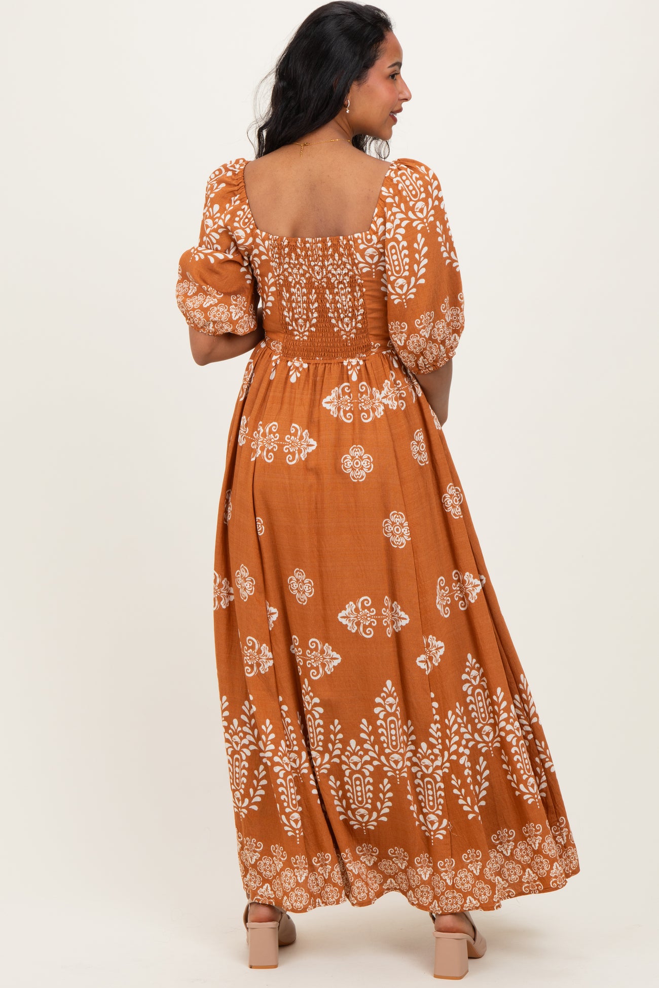 woman wearing a brown floral print maternity maxi dress with puff sleeves and a smocked bodice, showing a baby bump