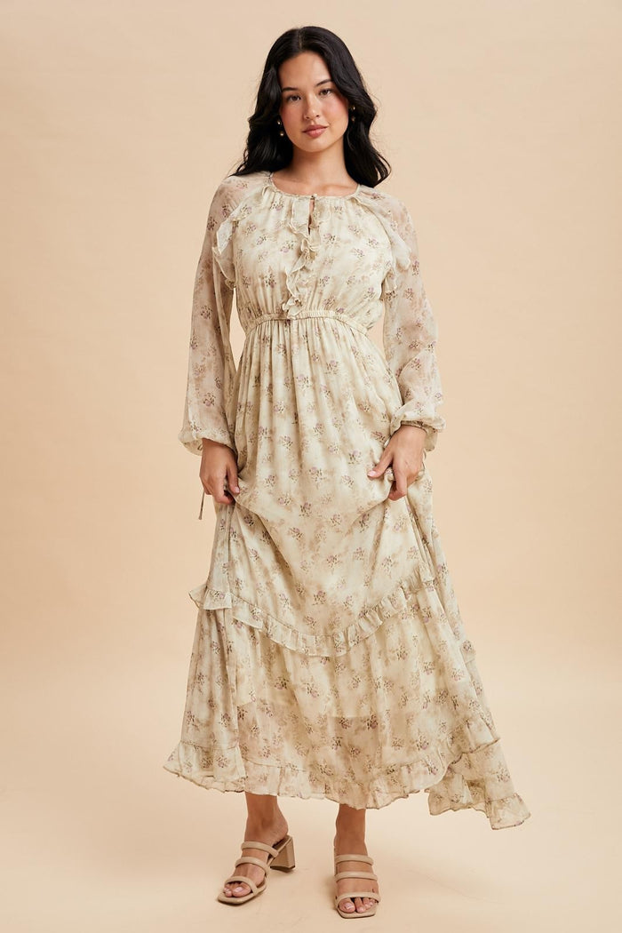woman wearing a cream floral maxi dress with ruffles and long sleeves, standing on a neutral background