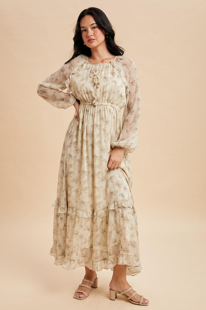 woman wearing a cream floral maxi dress with long sheer sleeves and ruffle details, standing on a beige background