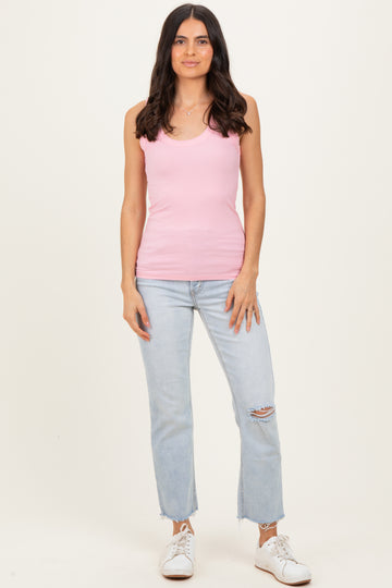 woman wearing a pink ribbed tank top and light blue ripped jeans, standing with a neutral background