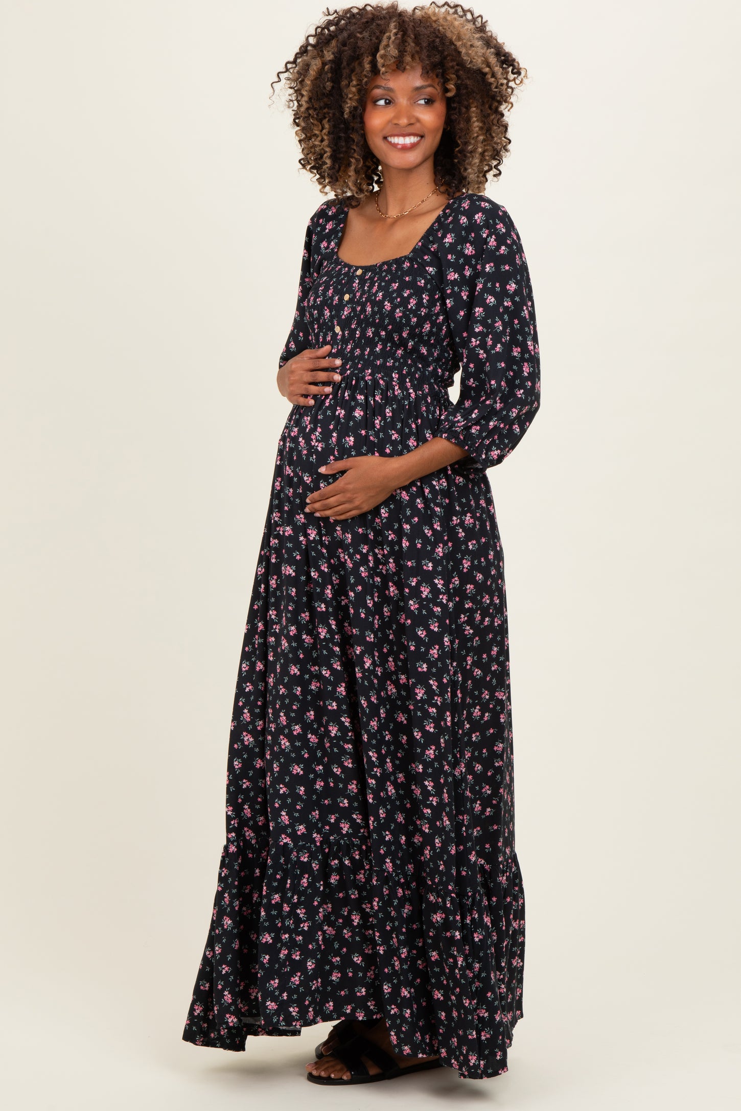 woman wearing a black floral maternity maxi dress with a square neckline and three-quarter sleeves, holding her baby bump