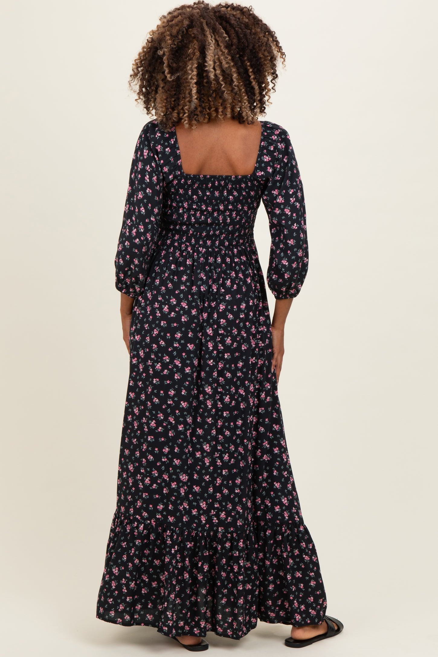 woman wearing a black floral maxi maternity dress with three-quarter sleeves and a tiered hem, showing her baby bump