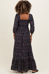 woman wearing a black floral maxi maternity dress with three-quarter sleeves and a tiered hem, showing her baby bump