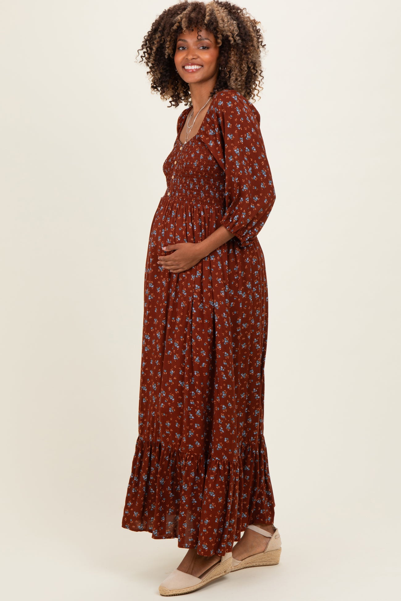 woman wearing a rust-colored floral maternity maxi dress with a smocked bodice and ruffled hem, showing her baby bump