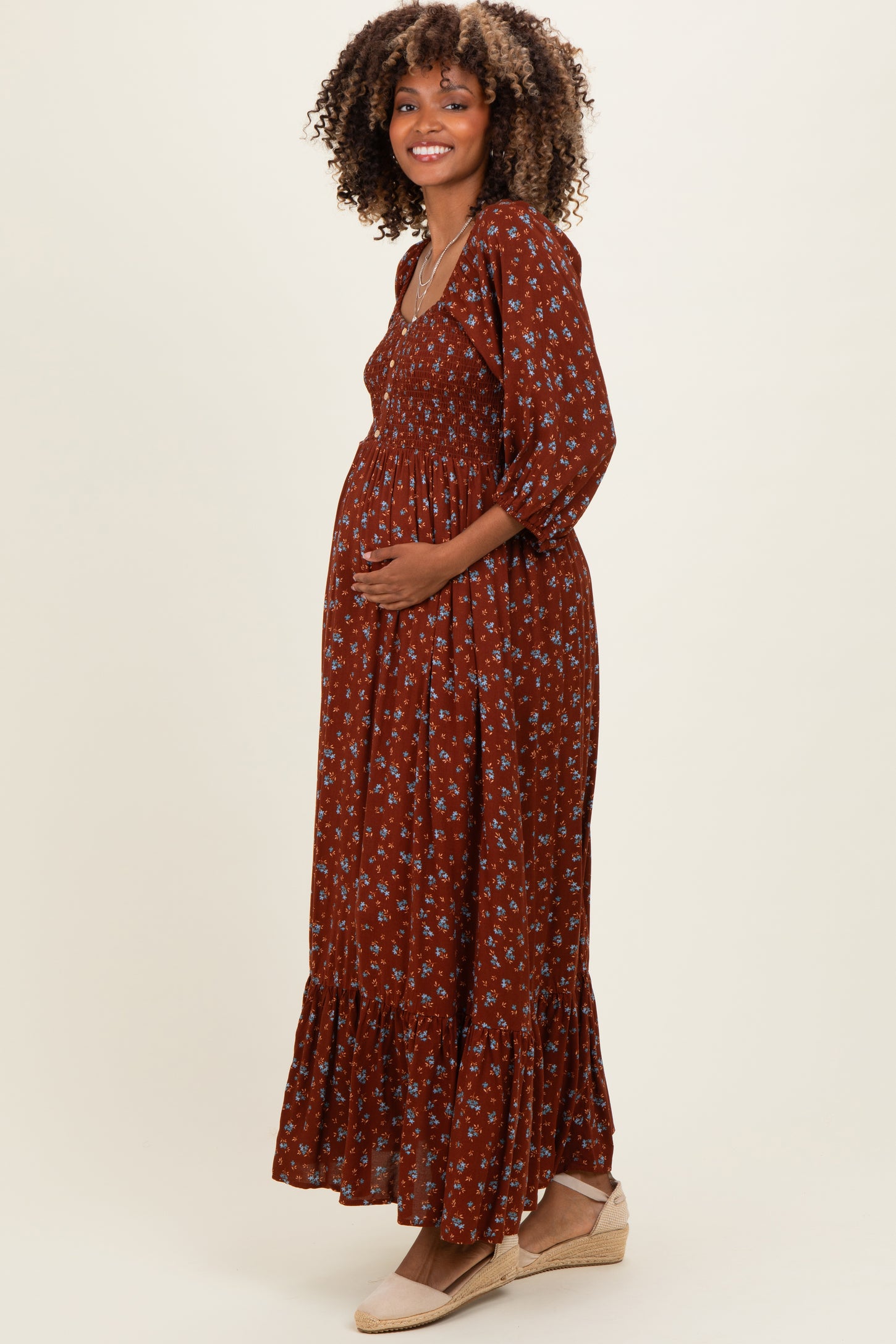 woman wearing a rust-colored floral maternity maxi dress with a smocked bodice and ruffled hem, showing her baby bump