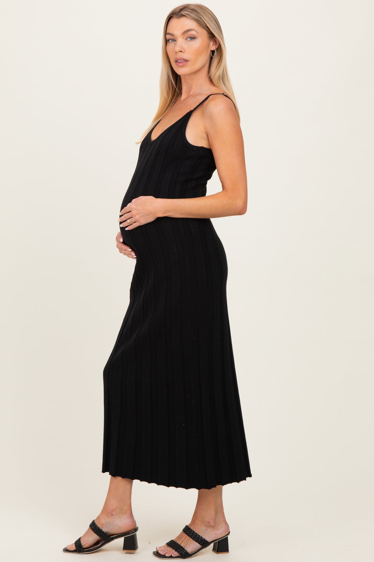 woman wearing a black ribbed maternity dress and cradling her baby bump